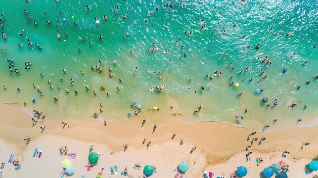 Top-down view capturing the lively atmosphere of a packed beach with people swimming in the sea and relaxing under colorful umbrellas on the sand..