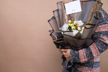 Side view of woman holding a bouquet of flowers over beige background with copy space