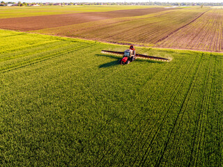 Drone shot of a tractor with sprayer in action on a vibrant green wheat farmland