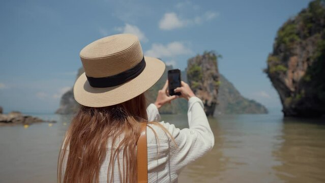 Woman travels on island Khao Phing Kan. Young female tourist sits on a boat and films take a photo of beautiful mountain landscape with a rock in the sea on smartphone. Travel, woman tourism concept.