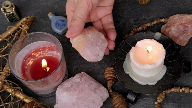 esoteric table, female fortuneteller's hand holding and using rose quartz stone, ambiance of mystical rituals, divination practices, symbolism associated with spiritualism and metaphysical exploration