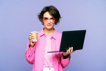 Portrait of beautiful smiling woman in sunglasses holding coffee cup and using laptop