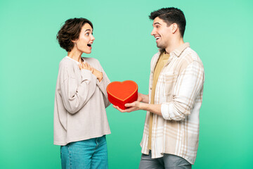 Smiling man giving gift box in heart shape to overjoyed beautiful woman