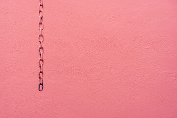Minimalistische Aufnahme einer rosa angemalten Regenablaufkette vor gleichfarbiger Fassade
