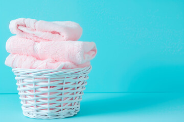Stack of clean towels in laundry wicker basket on blue background. The towels showcasing their soft and fluffy textures