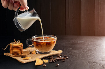 Milk cream poured into coffee cup, latte, cappuccino on wooden table black background and dark colors