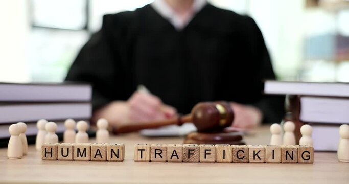 Word human trafficking and wooden men on table of judge with gavel in courtroom closeup 4k movie slow motion. Human trafficking and sexual slavery criminal liability concept