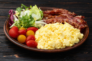 Breakfast plate . Scrambled eggs , bacon , cherry tomatoes and salad