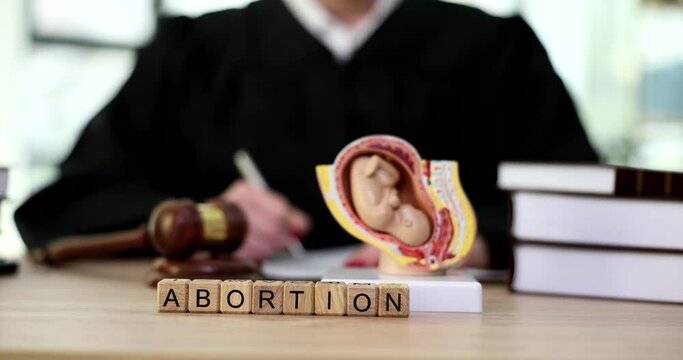 Model of fetus in uterus and word abortion on judge table closeup 4k movie slow motion. Official ban on abortion concept