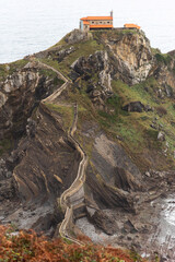 Vertical view of the tourist sanctuary of San Juan de Gaztelugatxe located on a hill in the middle of the sea with a beautiful stone staircase going up the cliff on a cloudy day.