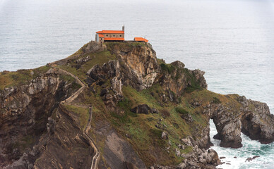 Panoramic view of the tourist sanctuary of San Juan de Gaztelugatxe located on a hill in the middle of the sea and surrounded by rocks with a beautiful stone staircase going up the cliff during cloudy