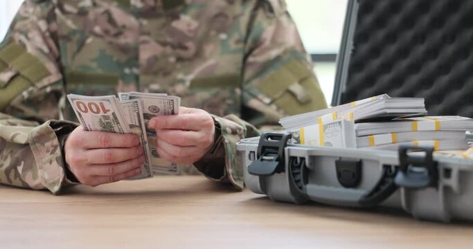 Military man counting dollar bills near suitcase with lot of money closeup 4k movie slow motion. Financing of military operations and supply of weapons concept