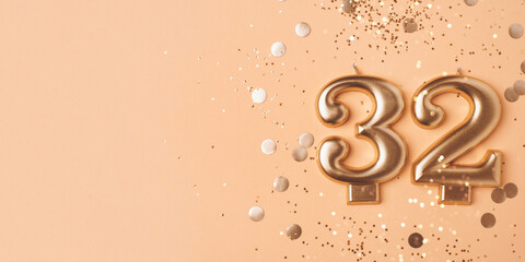 32 years celebration. Greeting banner. Gold candles in the form of number thirty one on peach background with confetti.