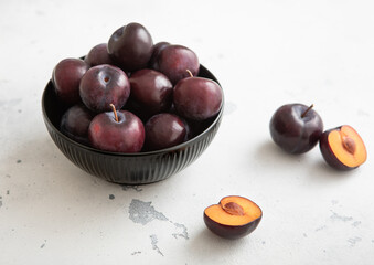 Bowl with raw ripe purple plums on light kitchen background.