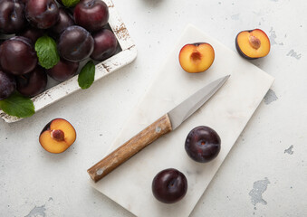 Wooden box of raw ripe purple plums on light kitchen background with kitchen knife.Top view.