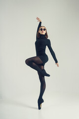a young ballerina in a black dress and sunglasses total black demonstrates choreography on pointe...