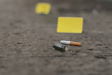 Pistol bullet shell on cement floor with blurred yellow paper and cigarette filter scraps background, concept for investigation and crime by police officers and investgators, soft focus.