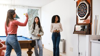 Happy diverse female friends playing dart in game room at home