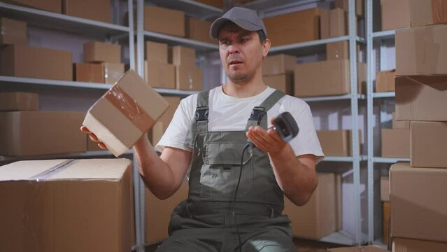 A confused man in a loader's uniform scans boxes with a barcode scanner and looks at the camera