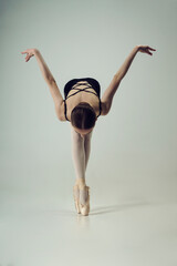 young teenage ballerina poses standing on her fingers in a tilt spreading her arms to the side