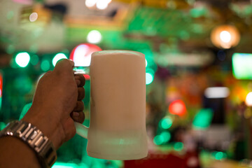 Hand holding beer in a frozen glass against the background of pub light blur background