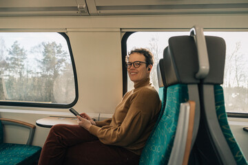 Woman smiling looking at the camera while traveling by train with smartphone in hand