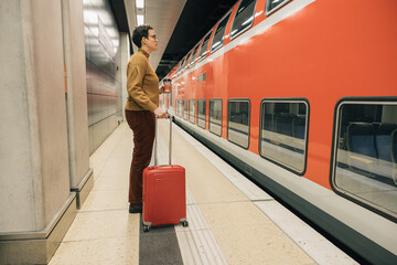 Woman with red suitcase and coffee in hand waiting for train at station