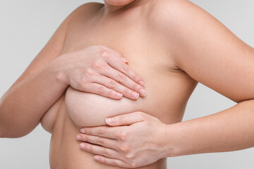 Obraz na płótnie Canvas Mammology. Naked woman doing breast self-examination on light grey background, closeup