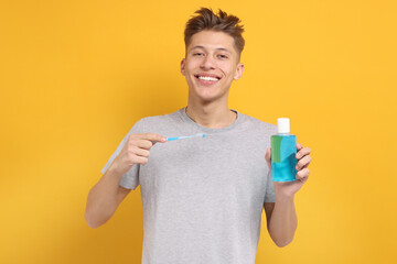 Young man with mouthwash and toothbrush on yellow background