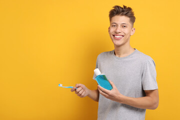 Young man with mouthwash and toothbrush on yellow background, space for text