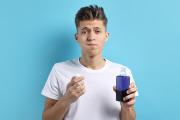 Young man using mouthwash on light blue background