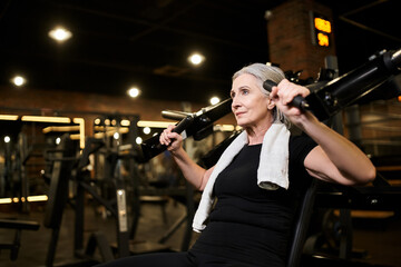Fototapeta na wymiar athletic attractive senior woman in sportswear exercising on chest press machine while in gym