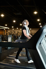 good looking mature jolly woman with gray hair and headphones exercising on treadmill in gym