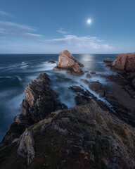 Landscape with natural sea arch and cliff in foreground in moonlight. Famous rock formation on the Moray Coast, Scottish Highlands, Scotland. Bow Fiddle Rock, long exposure.