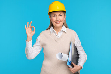 Architect in hard hat with draft and folder showing ok gesture on light blue background