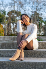 Relaxed Woman in White Sweater Dress Enjoying a Sunny Winter Day on Stone Steps