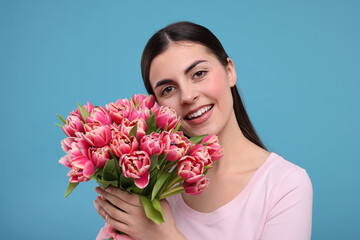 Happy young woman with beautiful bouquet on light blue background