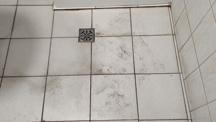 Old dirty tiled bathroom with shower and dirty floor with traces of shoes in a cheap hostel or...