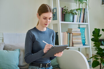 Young female teenager with digital tablet, stylus drawing illustrating sitting at home