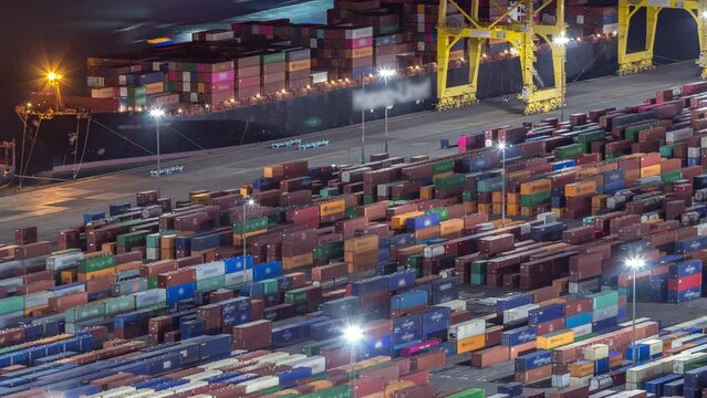 Night Timelapse of Barcelona's Seaport and Loading Docks. Aerial View from Montjuic Hill Showcases Illuminated Cranes and Multi-Colored Cargo Containers, Painting Port with a Dazzling Glow