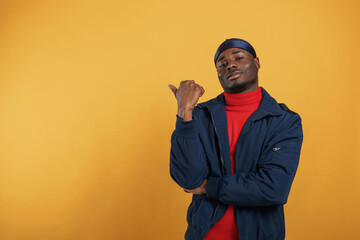 Showing something behind him by finger. Handsome black man is in the studio against yellow background - 777173006