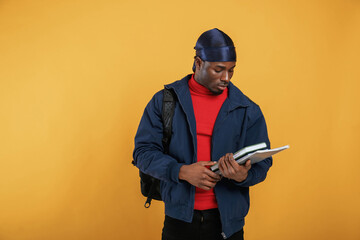 Student with books, backpack and notepad. Handsome black man is in the studio against yellow...