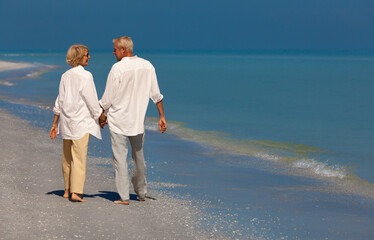 Happy senior couple walking smiling holding hands on an empty tropical beach - 777176290