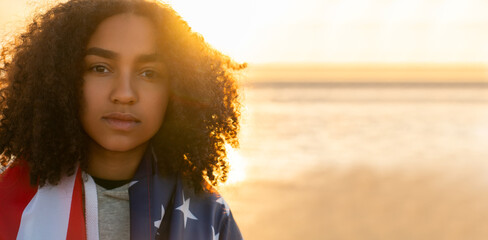African American Girl Teenager Wrapped in USA Flag on a Beach at Sunset - 777182612