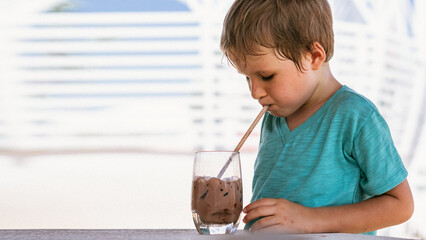 Happy childhood. Boy drinking chocolate tea with ice in hot summer day time. Cute lover of sweets...