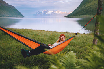 Woman tourist chilling in hammock travel in Norway healthy lifestyle summer vacations journey girl relaxing outdoor with sunset fjord and mountains view harmony with nature sustainable tourism - 777207037