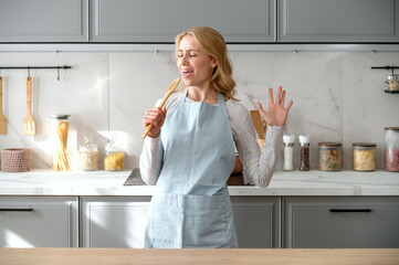 Happy housewife in apron singing excitedly with wooden spoon