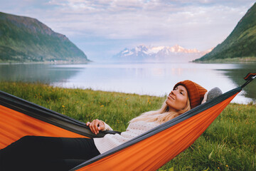 Woman chilling in hammock enjoying nature in Norway tourist traveling solo healthy lifestyle summer vacations with camping gear girl relaxing alone weekend getaway sunset fjord and mountains view - 777217256