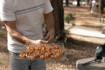 A man on a picnic holds a net with appetizing ready-to-grill meat and lays it out with tongs