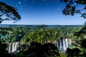Naklejka premium Enchanting View of Majestic Waterfalls in Lush Forest Under Starry Night Sky